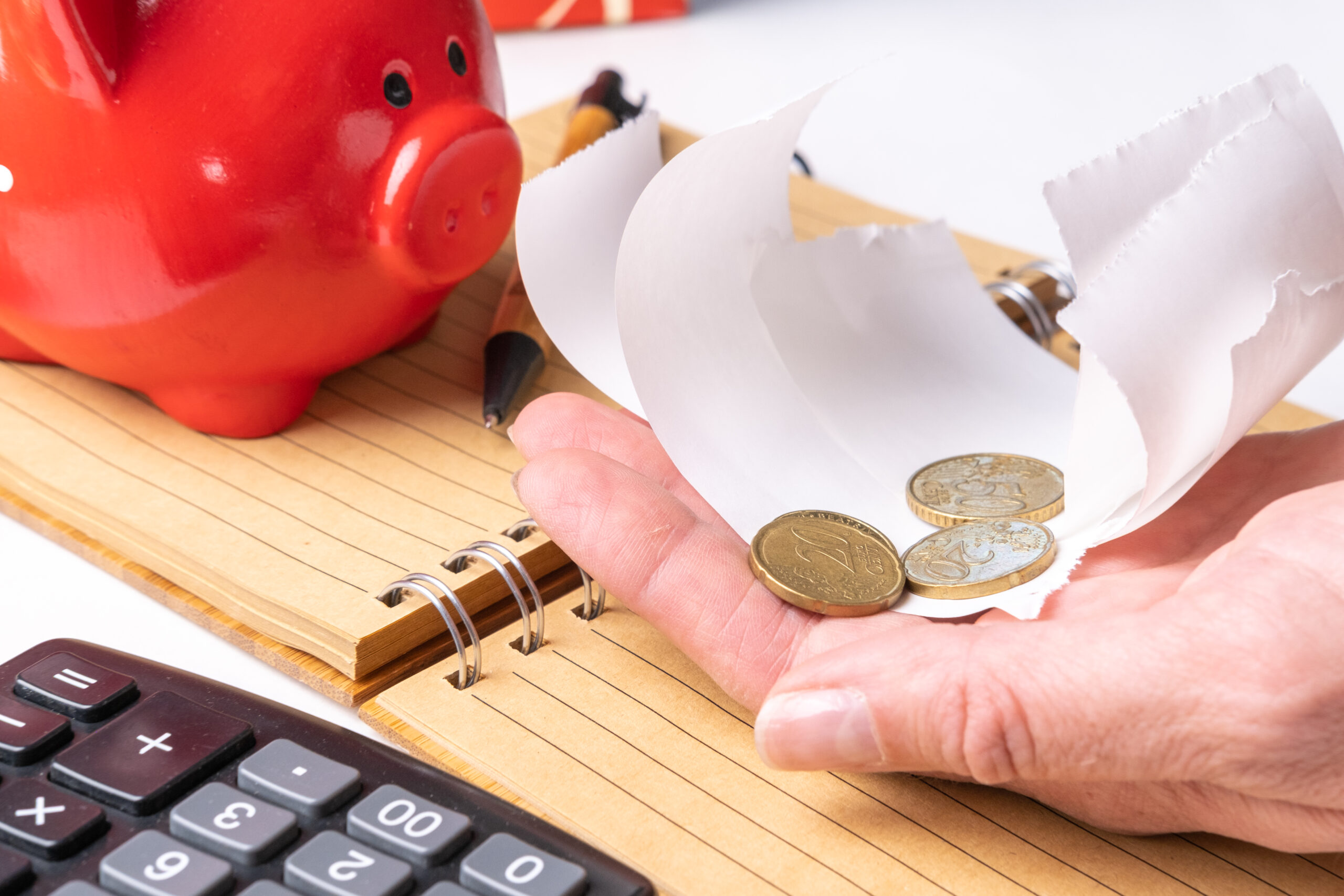 Mão segurando moedas com um porquinho quebrado